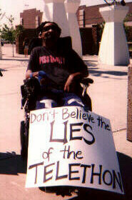 Photo of protester with sign saying "Don't Believe the Lies of the Telethon"; click to hear activists' response